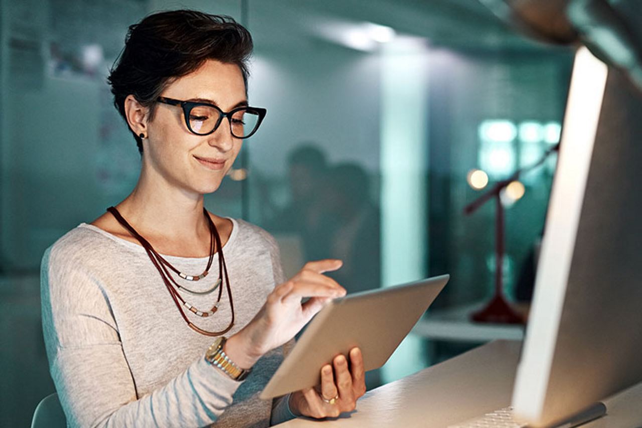 Female technician smiling while looking at her tablet screen in front of a computer