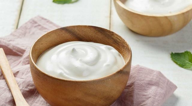 wooden bowl with yogurt inside on a table with placemat and spoon