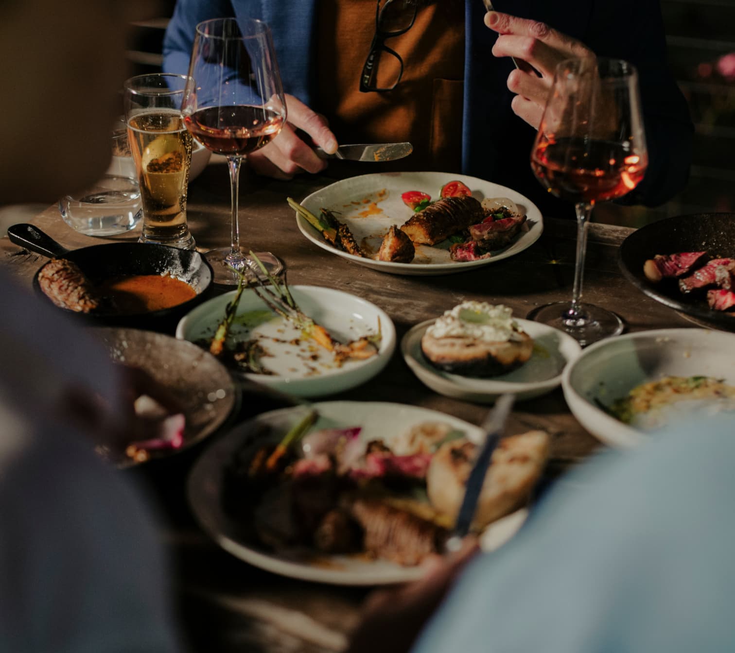 Food and Wine on a wooden dining table. Patrons of the meal share many plates of different dishes.