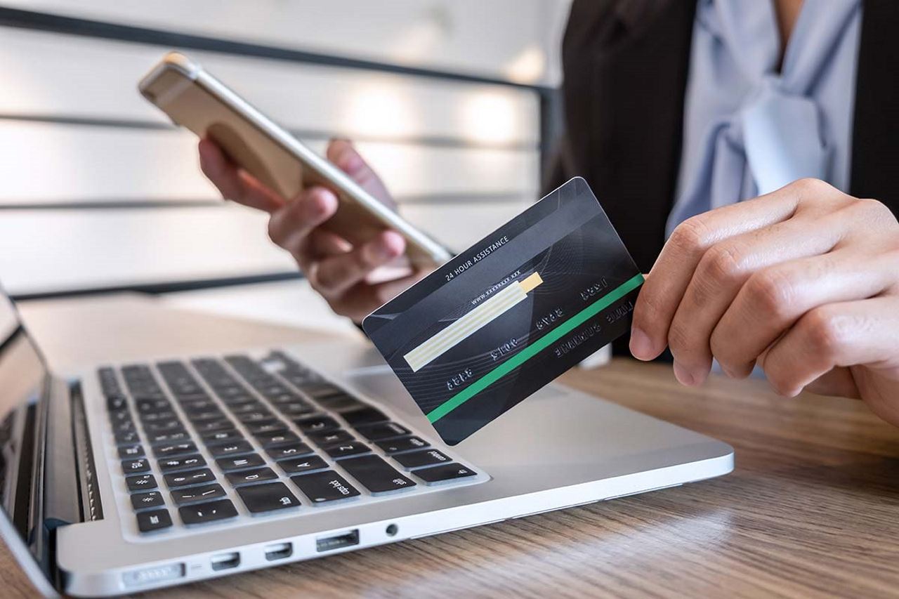 hands holding credit card and phone in front of laptop